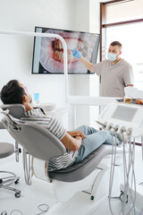 Obraz premium Dentist discussing with laying patient showing the image of his teeth on the screen