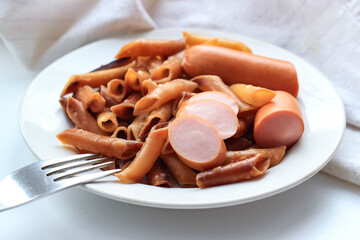 Macaroni, fried and cooked, in a white plate with a sliced sausage. A hearty lunch.