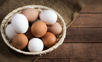 wicker wooden plate with brown and white eggs on a brown wooden background with burlap