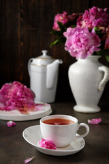 Fototapeta na wymiar tea in a white porcelain cup on a black table with a bouquet of peonies. Hot drink on a dark background. Concept
