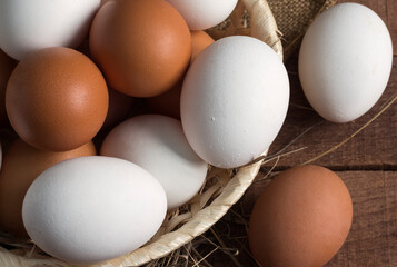 wicker wooden plate with brown and white eggs on a wooden background, top view