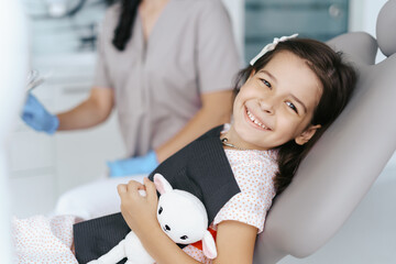 Cute little girl sitting on a modern dental chair and having dental consultation with dentist