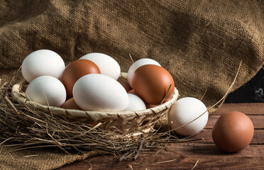 wicker wooden plate, in hay with brown and white eggs on a brown wooden background with burlap