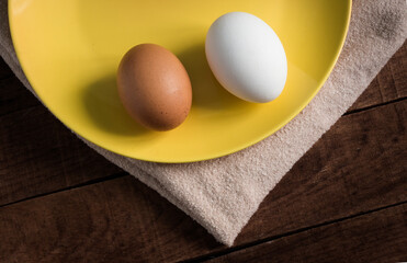 two chicken eggs in a yellow plate on a wooden background
