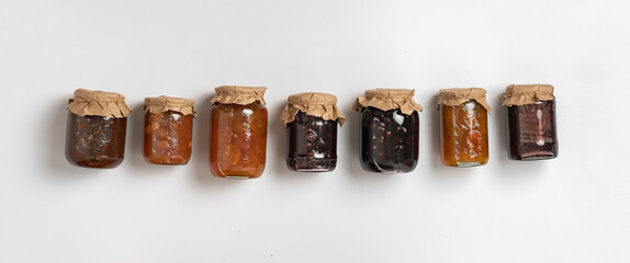 the row of glass jar with jam made of homemade cherry and fruit on color background, various mix