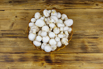 Fototapeta na wymiar Fresh champignon mushrooms in wicker basket on the wooden table. Top view