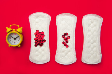 Menstrual pads with bright red glitter and alarm on red background. Woman periods cycle, menstruation frequency. Minimalist still life photography concept.
