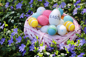 Easter.Pink wicker nest with easter decorative eggs in purple spring flowers.Easter eggs in a basket in the garden.Spring Religious Holiday Symbol. festive easter background