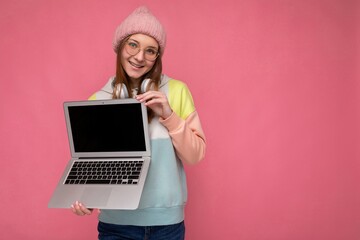 Photo of beautiful young girl holding computer laptop looking at camera isolated over colourful background