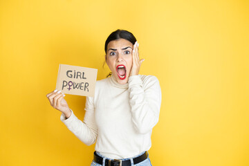 Young beautiful activist woman protesting holding poster with girl power message crazy and scared...