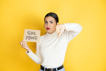 Young beautiful activist woman protesting holding poster with girl power message with angry face, negative sign showing dislike with thumb down