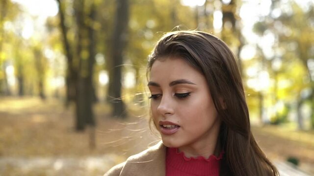 Attractive brunette poses with her long hair and looks at camera in autumn park