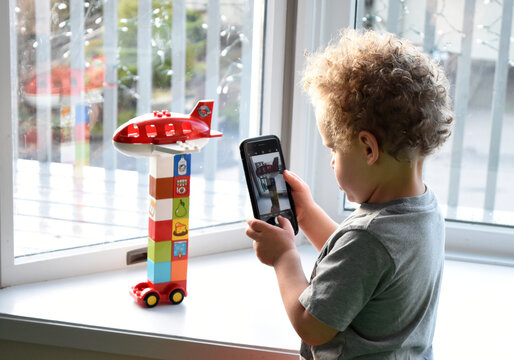 3 year old boy using cell phone to take pictures of his blocks creation.