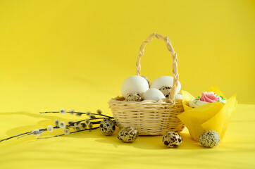 Eggs in white wicker basket and pussy willow branches, Quail eggs, easter cake on yellow background with copy space. Happy Easter concept, Easter table.