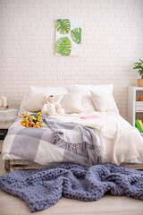 cozy bed with light linens and knitted blankets. Bright bedroom with lots of indoor plants and home decor.The concept of home comfort and recreation.