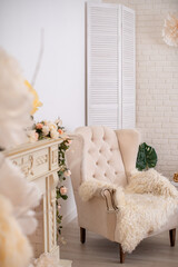 elegant chic fireplace, the color of white chocolate, decorated with flowers and candles, and a light velour chair. Spring romantic decoration with a fireplace portal with artificial flowers.