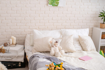 cozy bed with light linens and a teddy bear and a knitted blanket made of merino yarn. Bright bedroom with lots of indoor plants and home decor.The concept of home comfort and relaxation.