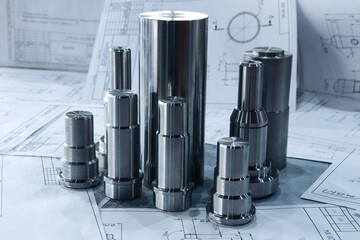 Products manufactured on metal-working machines lie against the background of production drawings, close-up. 