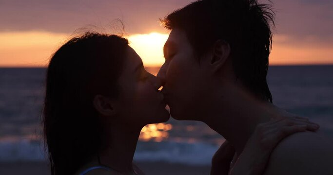 Take a close-up shot of a teenager, a woman kissing with her boyfriend on the beach, with the golden glow of the evening sun. Concept pictures about love, romance, Valentine, propose. 4K.