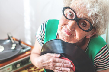 Elderly pretty woman with glasses listens to vinyl records on a turntable. Retro music. Grandma is...