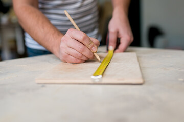 Close-up of man workers hand measuring a wooden board with a ruler with scale. Joinery work on the production of wooden furniture. Small Business Concept