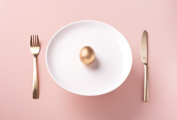 On a white plate lies a golden egg, next to golden cutlery on a powdery background, festive Easter setting, horizontal orientation, copy space