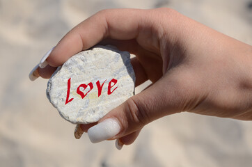 female hand helds a white stone with the inscription "Love"