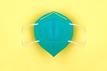 Green FFP2 n95 protective face mask on yellow background. Protection and prevention against coronavirus, covid-19 and other viruses.	