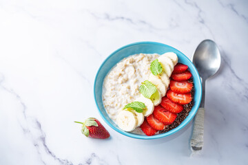 Oatmeal porridge with milk and fresh strawberries and banana slices in a blue bowl