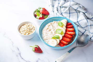 Oatmeal porridge with milk and fresh strawberries and banana slices in a blue bowl