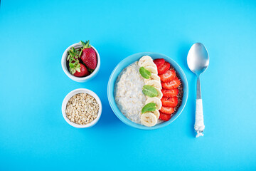 Oatmeal porridge with milk and fresh strawberries and banana slices in a blue bowl