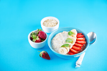 Oatmeal porridge with milk and fresh strawberries and banana slices in a blue bowl