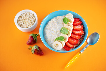 Oatmeal porridge with milk and fresh strawberries and banana slices in a blue bowl