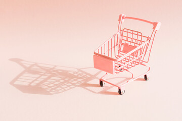 Empty mini pink shopping trolley with shadow on pink background. Minimalist style. Black Friday, season sale, discount concept.