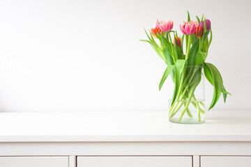 Fresh bright bouquet of colorful Tulips near white wall on wooden shelf in glass vase wit space for text, Spring, April, decoration interion concept modern design. Copy space