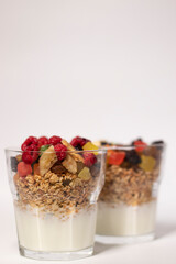 muesli dessert with yogurt and candied or dried fruits with raspberries on top in glass isolated on white background. Granola breakfast