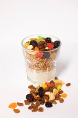 muesli dessert in glass with yogurt and candied or dried fruits with raspberries on top, isolated on white background. raisins, nuts and candied fruits nearby. Granola breakfast