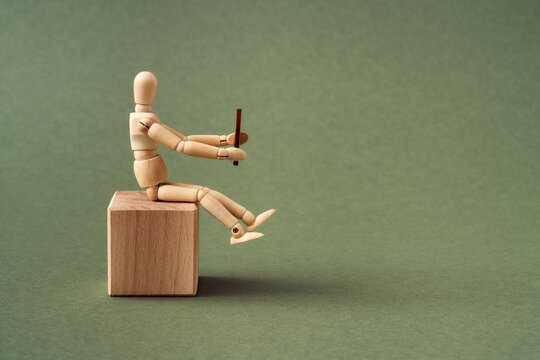 Wooden Figure Sitting On A Cube And Holding A Wheel As If Driving A Car