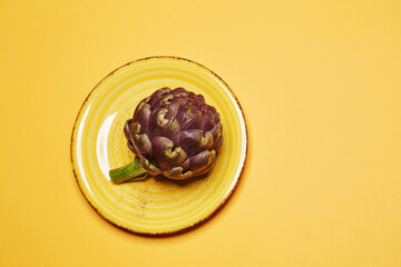 Fresh ripe raw artichoke on the yellow ceramic plate isolated on the bright solid yellow fond background