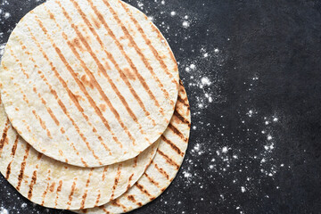 Grilled tortilla. Mexican flatbread - tortilla on a black concrete background with flour.