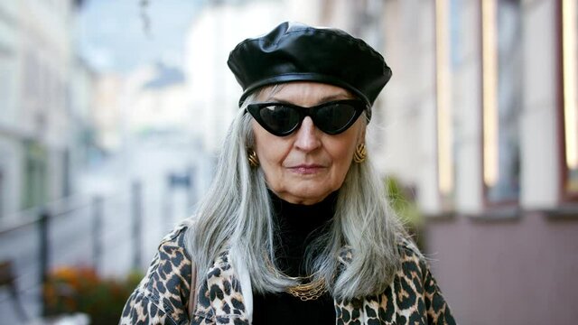 Senior chic woman with sunglasses standing outdoors, looking at camera.