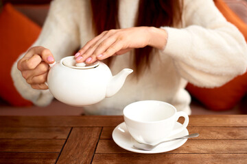 Fototapeta na wymiar female hands pouring tea from teapot into a white cup on wooden table