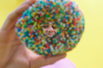 Smiling man holding a donut on a yellow background