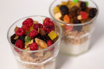 muesli dessert with yogurt and candied or dried fruits with raspberries on top in glass isolated on white background. Granola breakfast