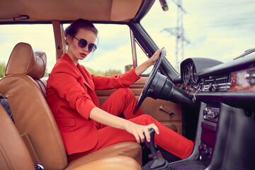 Beautiful young woman wearing red costume and sunglasses sitting in retro car