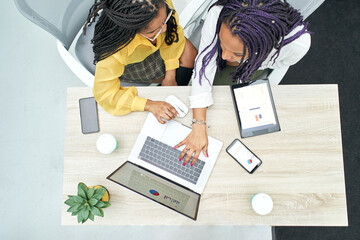 Top view of two young black women working in the office. Reviewing analytical data on various...