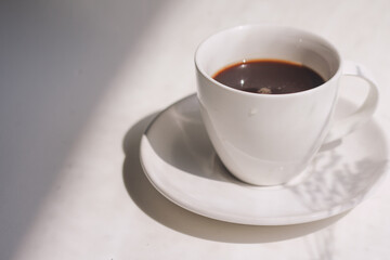 Cup of hot coffee on white background and organic shadow overlay on white texture background, copy space. close-up top view. minimal, modern style. window of cafe.