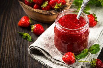 Strawberry jam in the glass jar with fresh berries at wooden table.