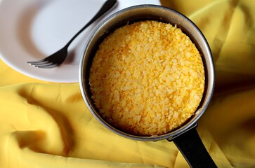 Couscous in the pan, with plate and fork in the background. Brazilian Couscous (Cuscuz Brasileiro). Typical Brazilian Northeast breakfast.
