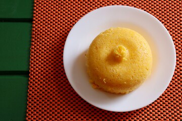 Brazilian Couscous (Cuscuz Brasileiro) on green and orange background. Brazilian breakfast concept. Cornmeal.
